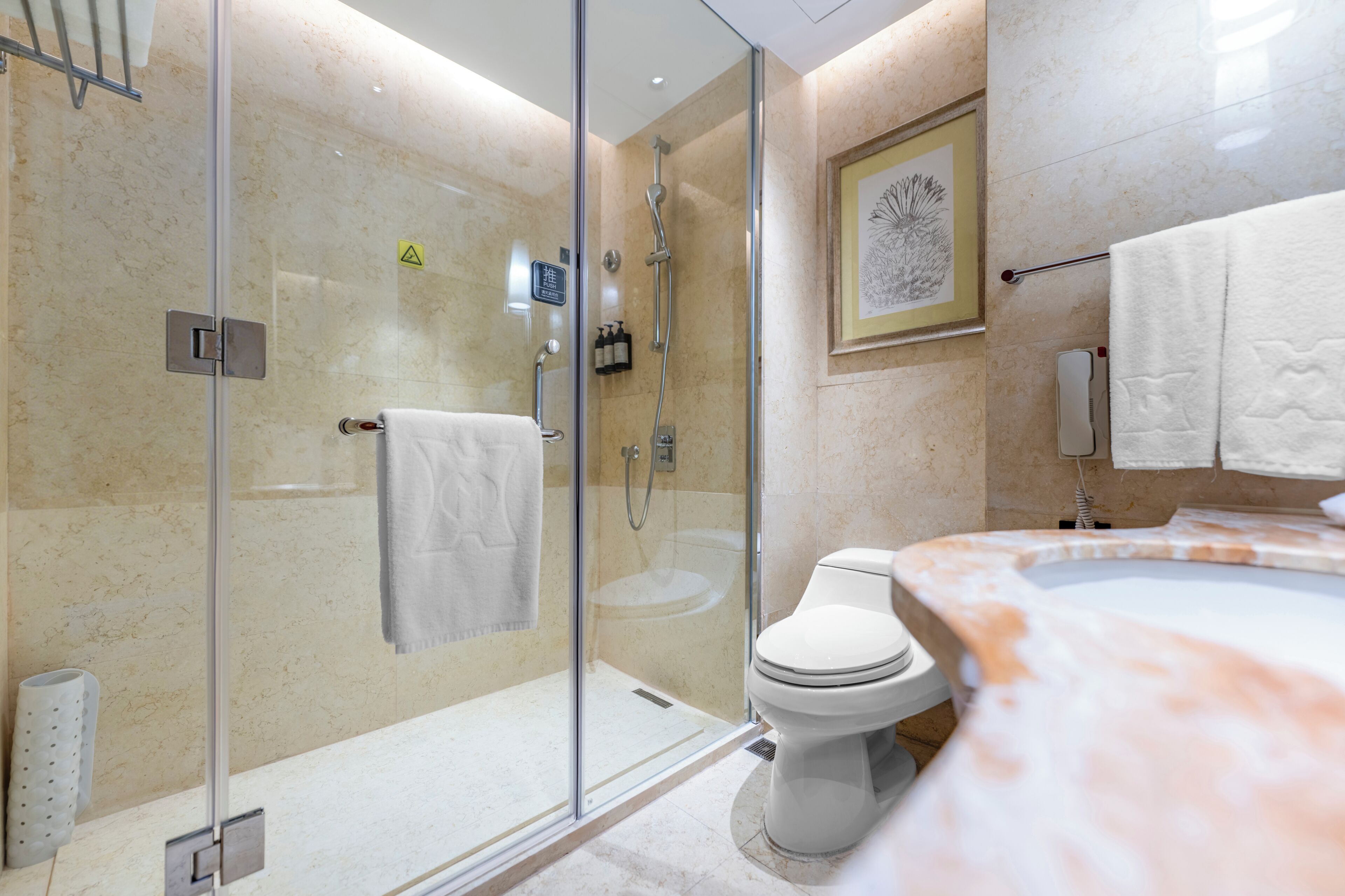 Een moderne badkamer met een douchecabine van glas, een wit toilet en een marmeren wastafel.