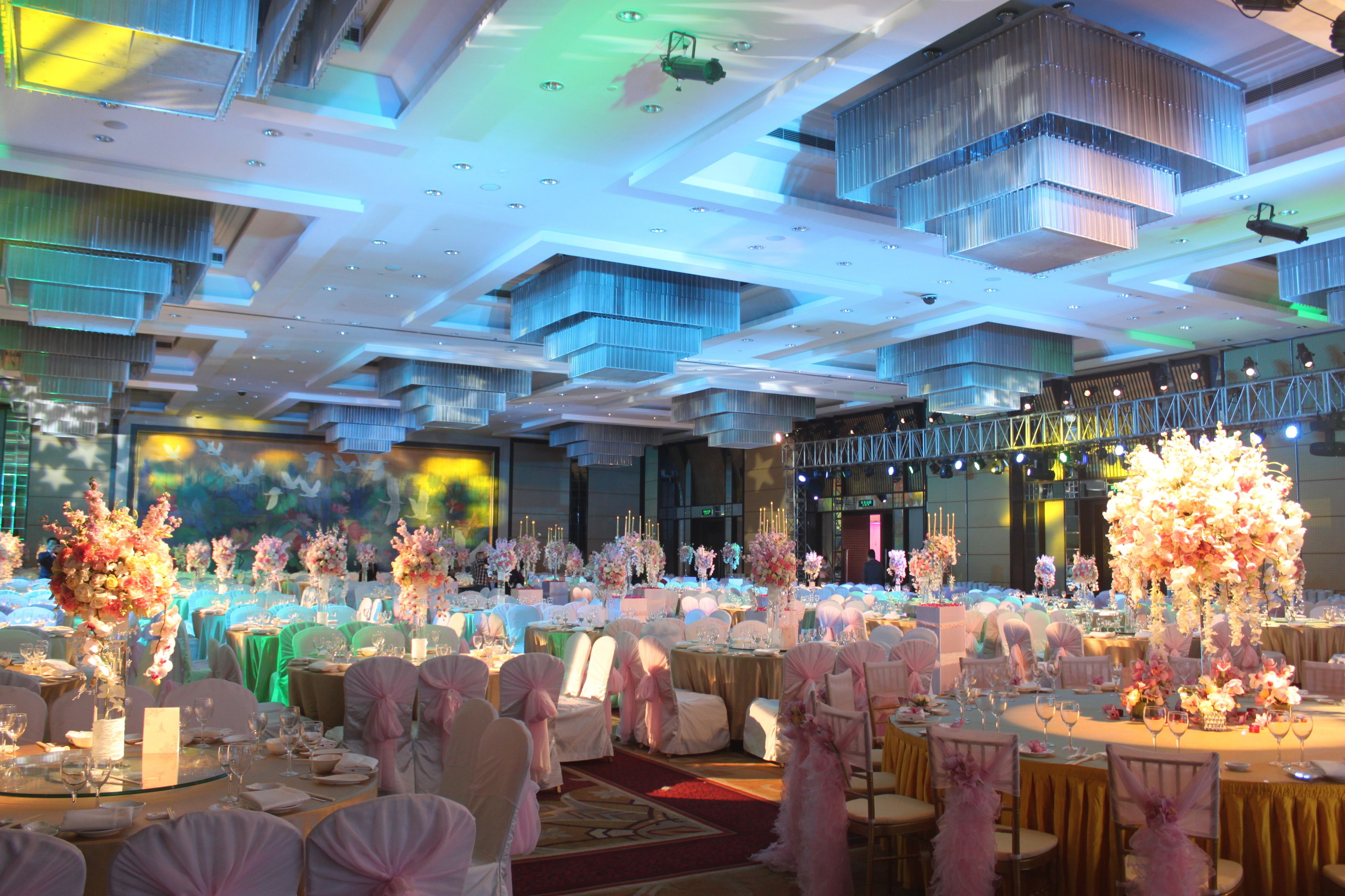 Un salón de banquetes con mesas redondas, sillas blancas y centros de mesa florales.