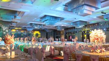 Un salón de banquetes con mesas redondas, sillas blancas y centros de mesa florales.