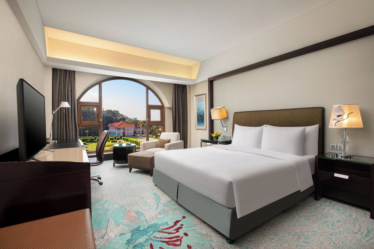 A hotel room with a large bed, a desk, a chair, and a view of the outdoors.