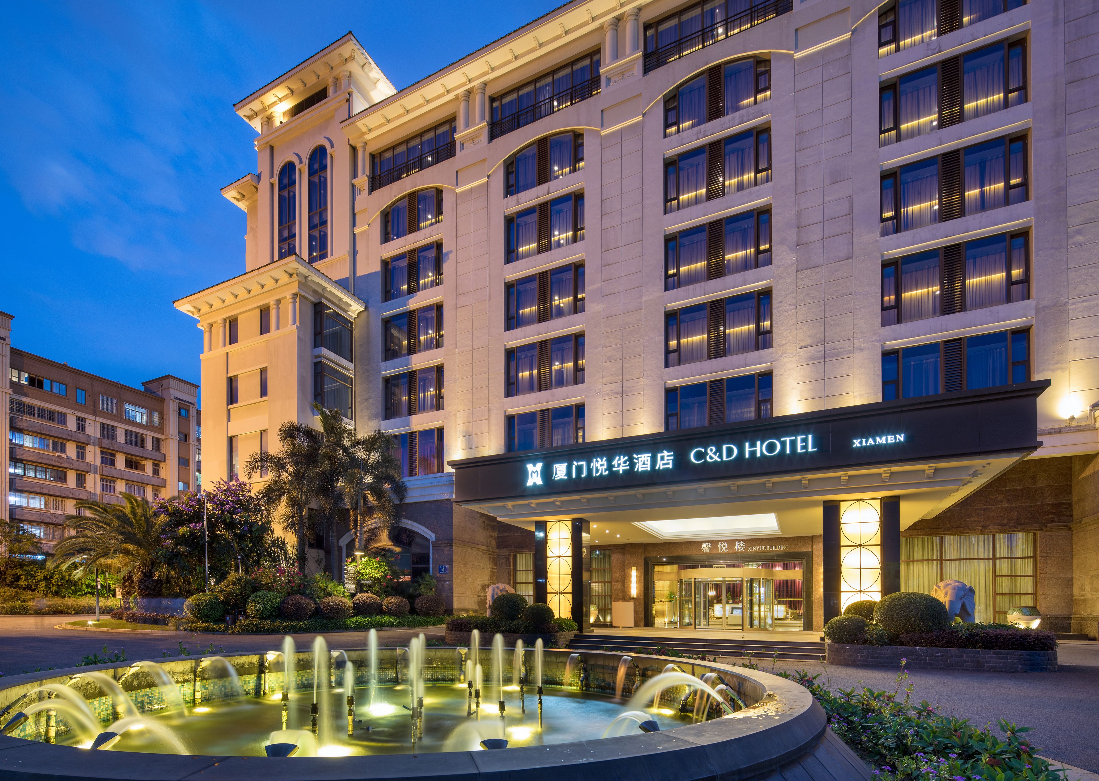 A hotel with a large fountain in front, multiple floors, and a well-lit entrance.