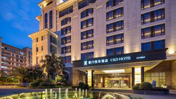 A hotel with a large fountain in front, multiple floors, and a well-lit entrance.
