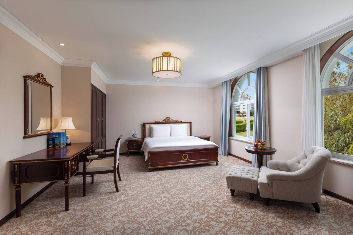 A hotel room with a large bed, a desk, a chair, and a small table.