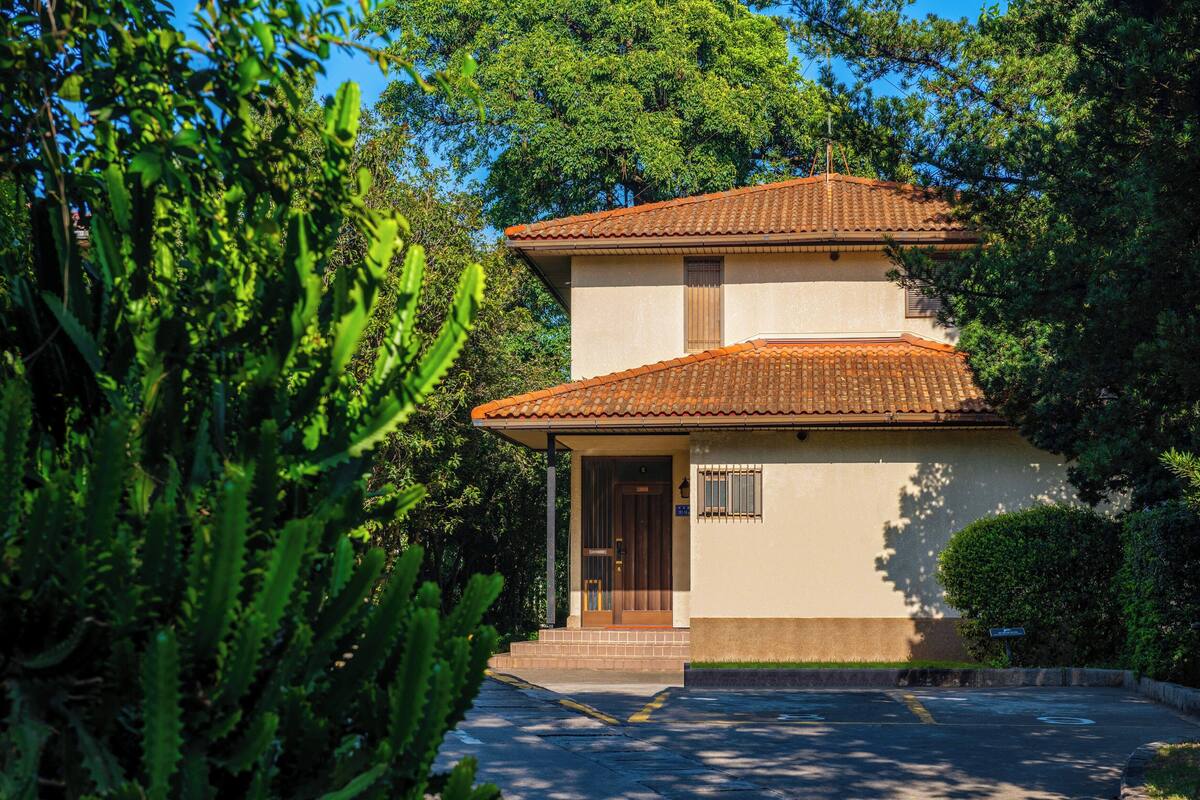 A two-story building with a tiled roof, surrounded by lush greenery.