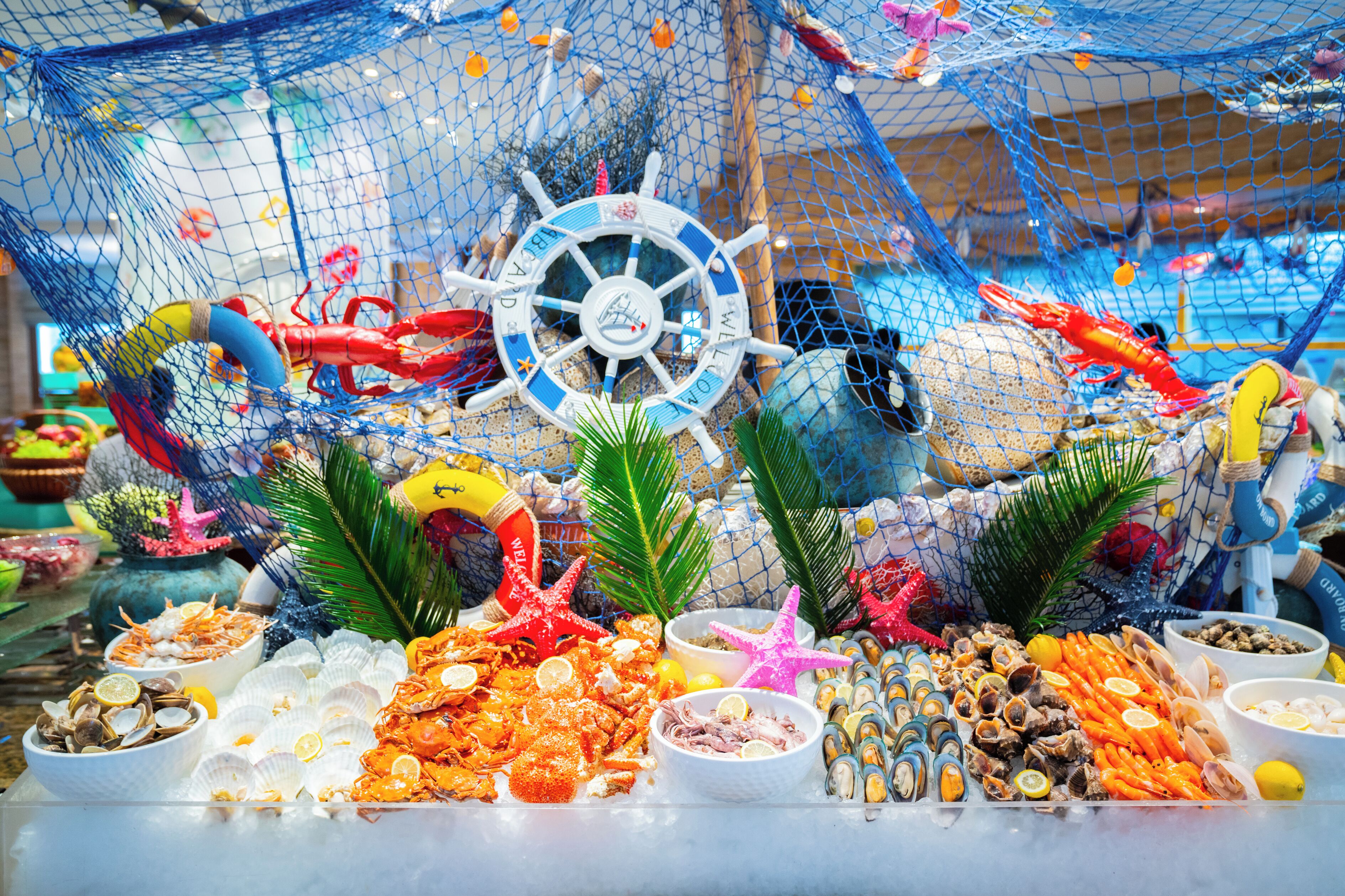 A seafood buffet with various shellfish and seafood dishes, a ship's wheel decoration, and starfish.
