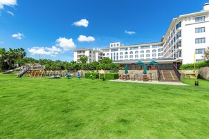 A hotel with a large grassy courtyard, outdoor seating area, and a playground.