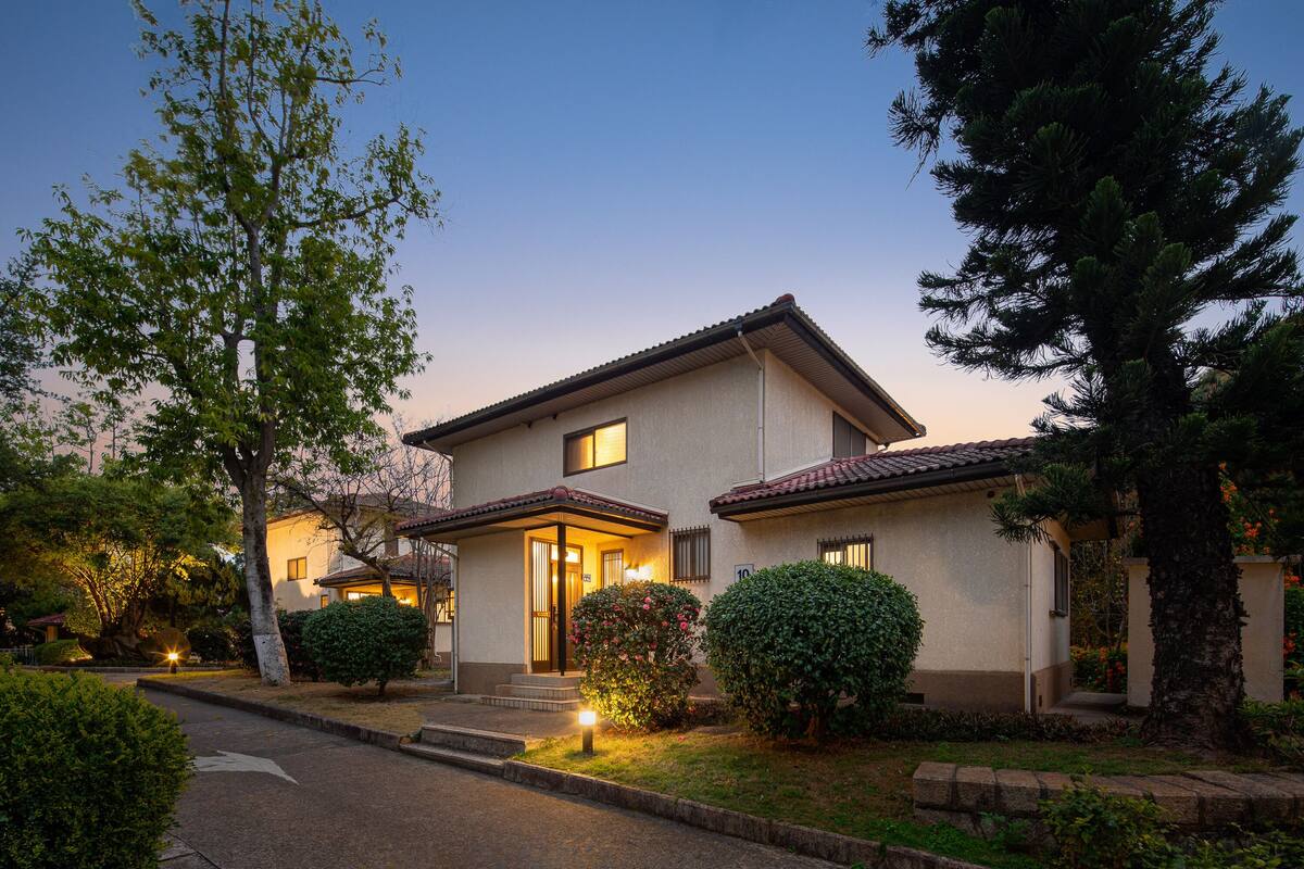 A two-story house with a front porch, a small garden, and a well-maintained lawn.