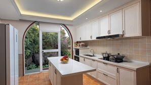 Una cocina moderna con muebles blancos, una isla central y vistas a un jardín a través de un arco.