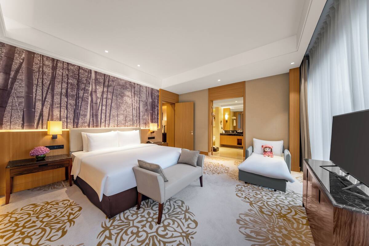 A hotel room with a large bed, a sofa, a TV, and a bathroom visible through an open door.