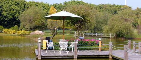 A wooden dock with white metal chairs and a green umbrella.