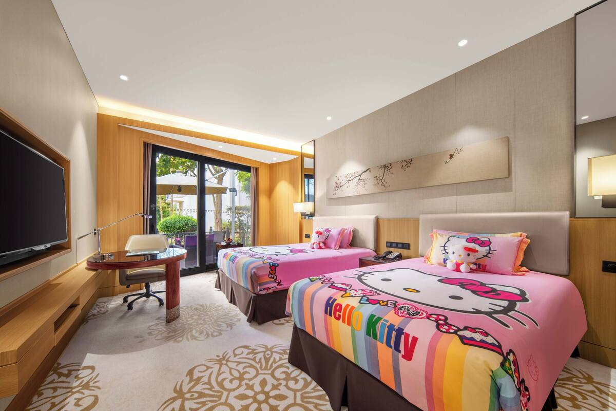A hotel room with two beds, a TV, a desk, and a view of the outdoors.