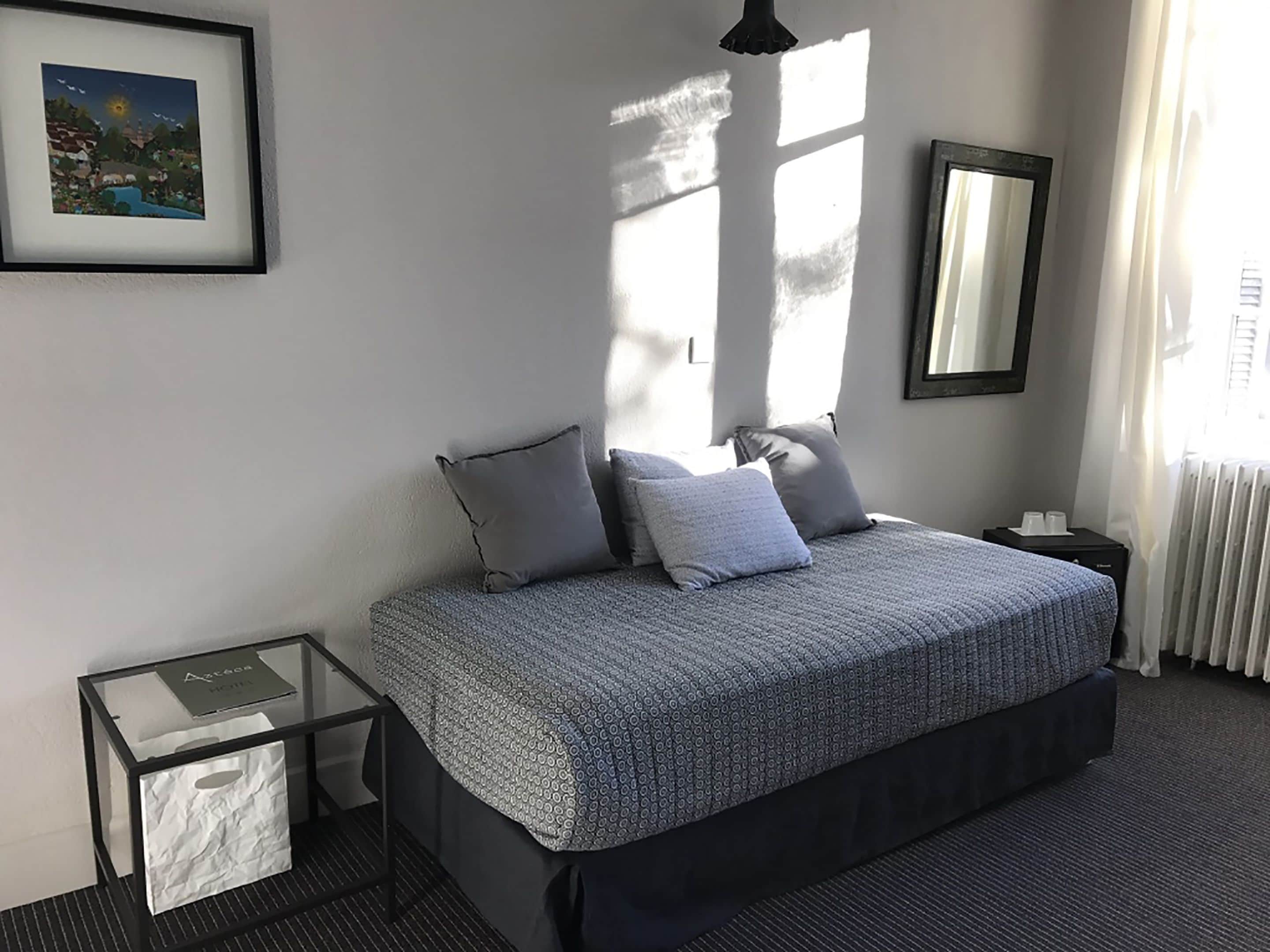 Een slaapkamer met een bed, nachtkastjes, een lijst met een afbeelding en een raam met gordijnen.