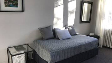 Een slaapkamer met een bed, nachtkastjes, een lijst met een afbeelding en een raam met gordijnen.