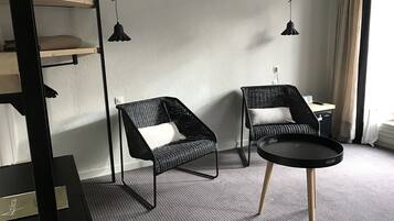 Ein modernes Hotelzimmer mit zwei schwarzen Korbstühlen, einem runden schwarzen Tisch und einem Bett mit weißer Bettwäsche.