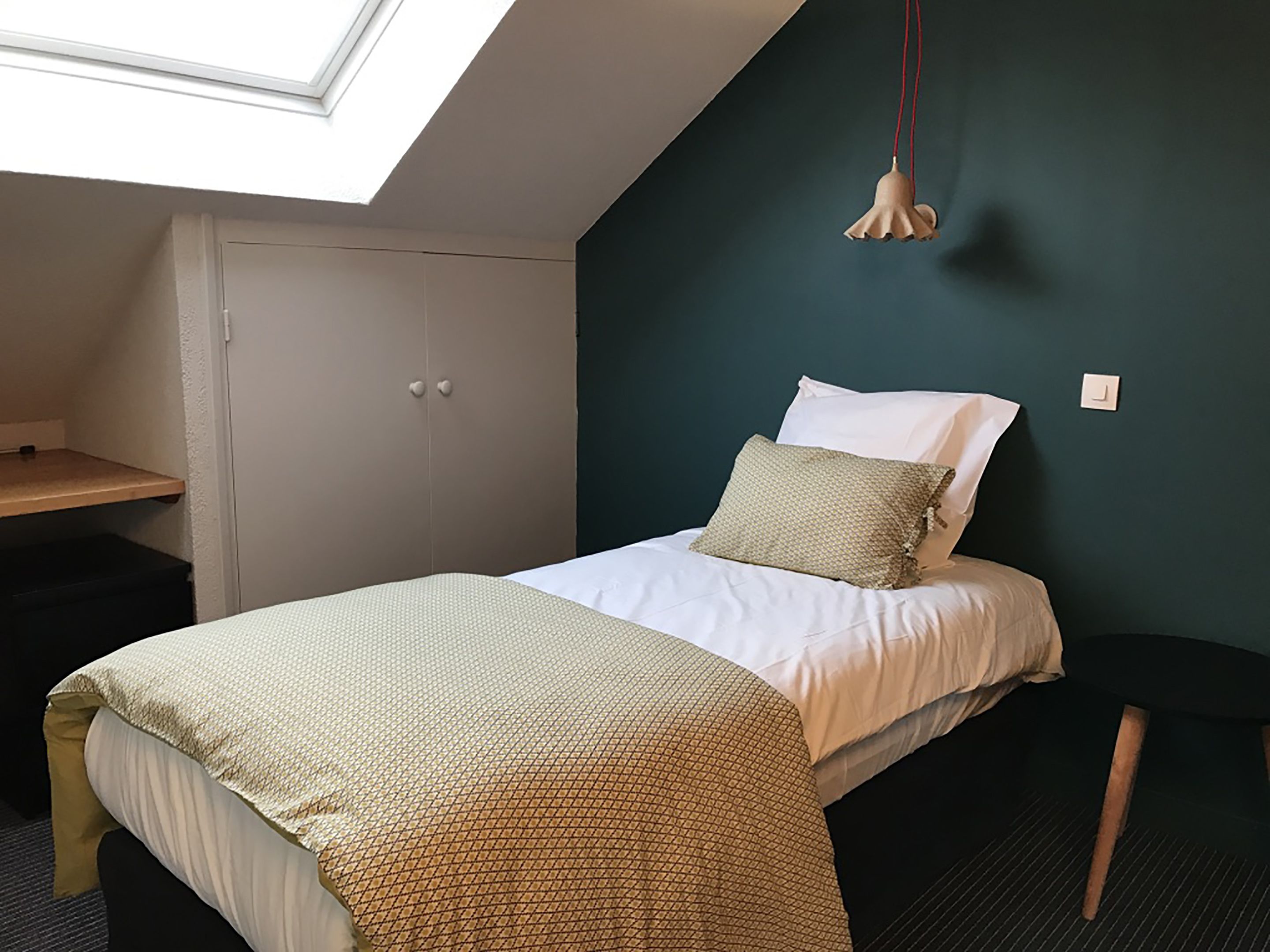 A bedroom with a bed, a desk, a wardrobe, and a skylight.