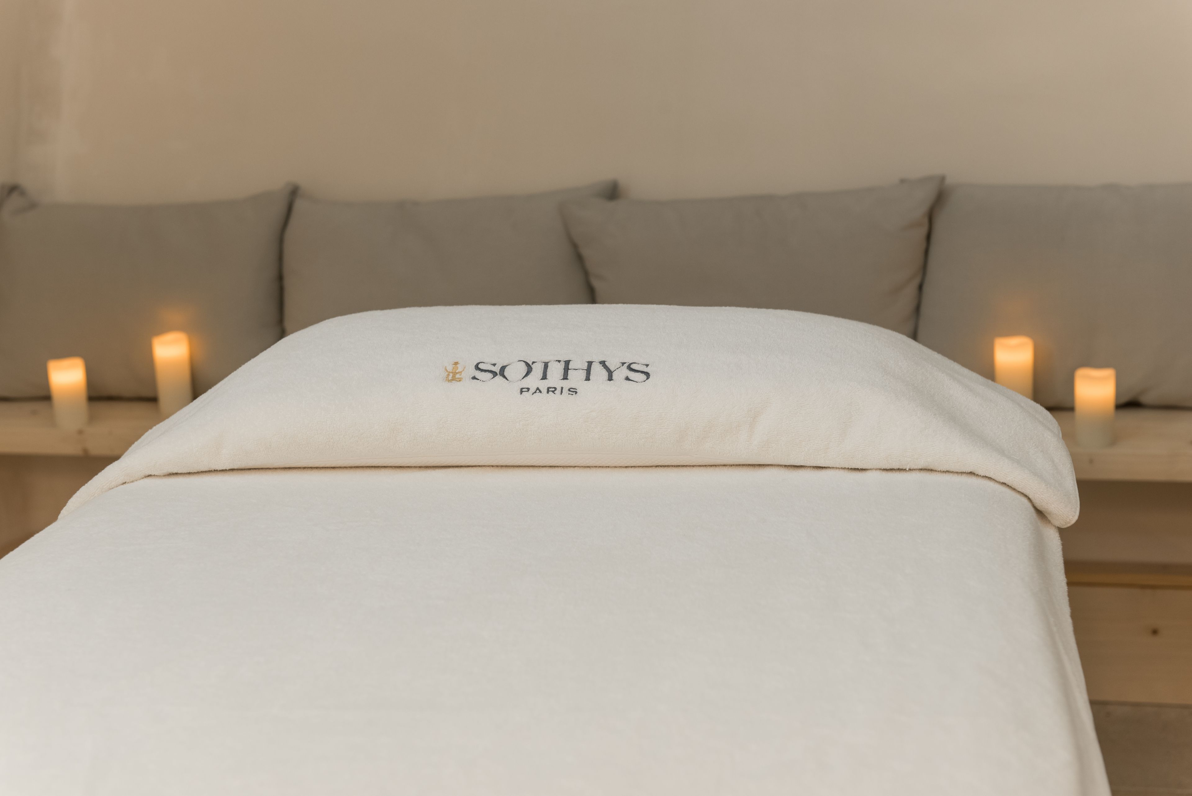 A bed with a white pillow labeled "SOTHYS PARIS" and a beige headboard.