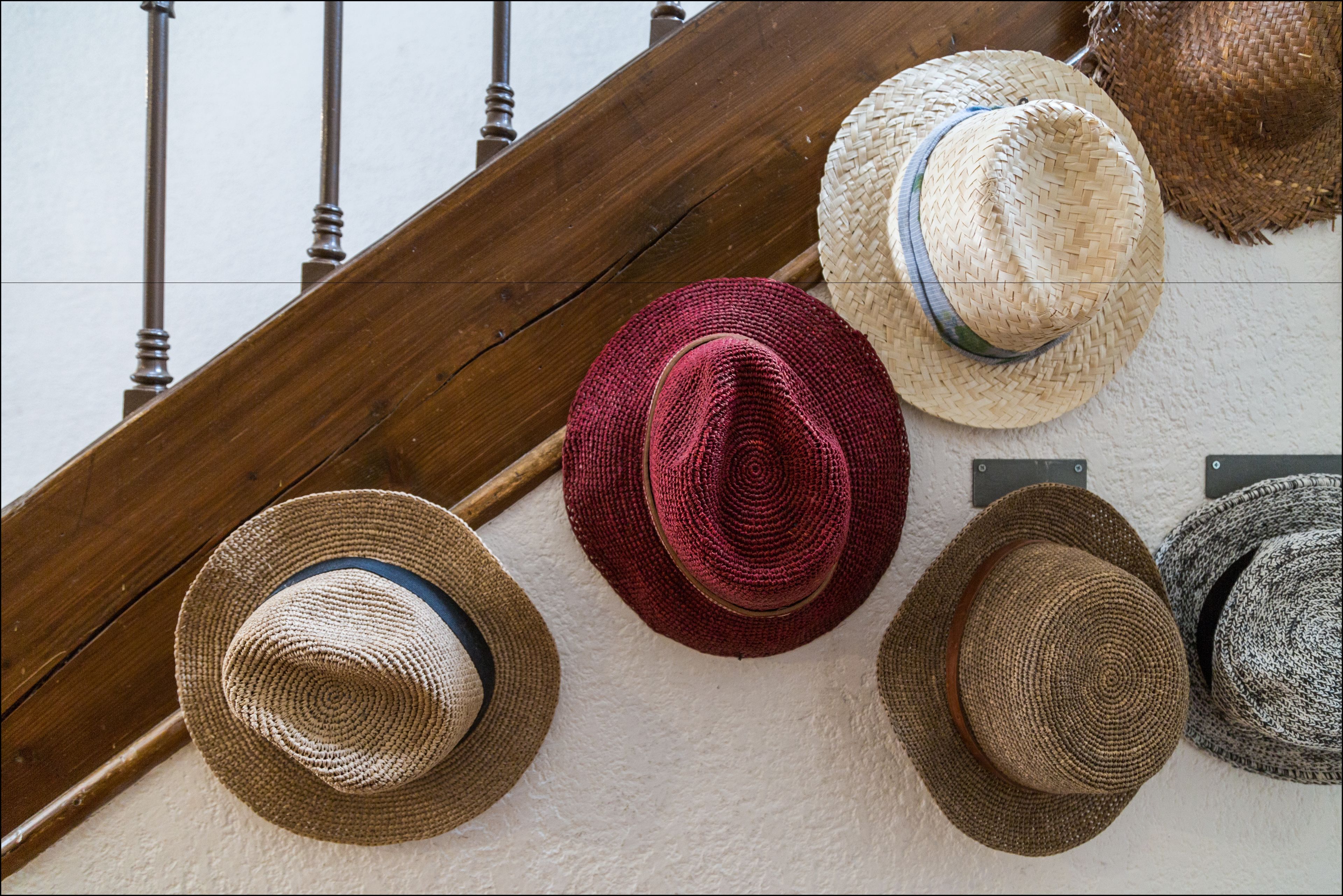 A staircase with a wooden handrail and a wall with various hats displayed.