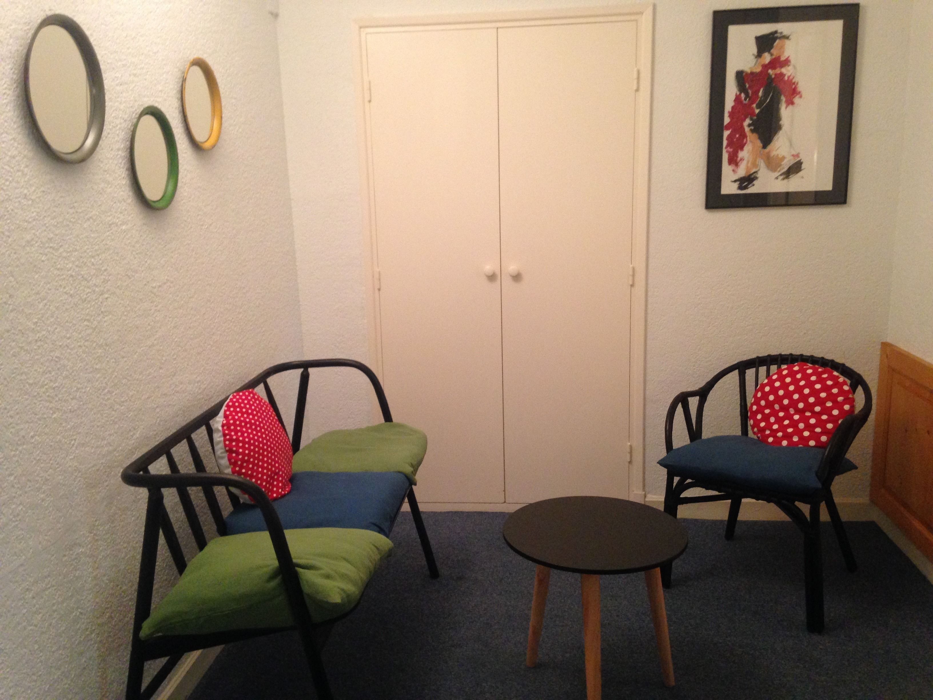 Una habitación con dos sillas negras con cojines verdes y rojos, una mesa redonda pequeña y una puerta blanca. Encima de la puerta hay tres adornos circulares en la pared.