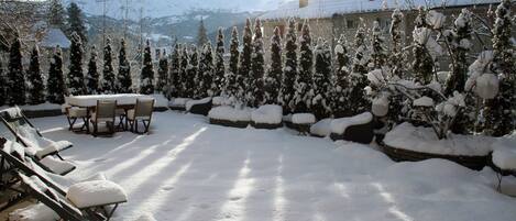 Un área de estar al aire libre cubierta de nieve con vistas a montañas nevadas al fondo.