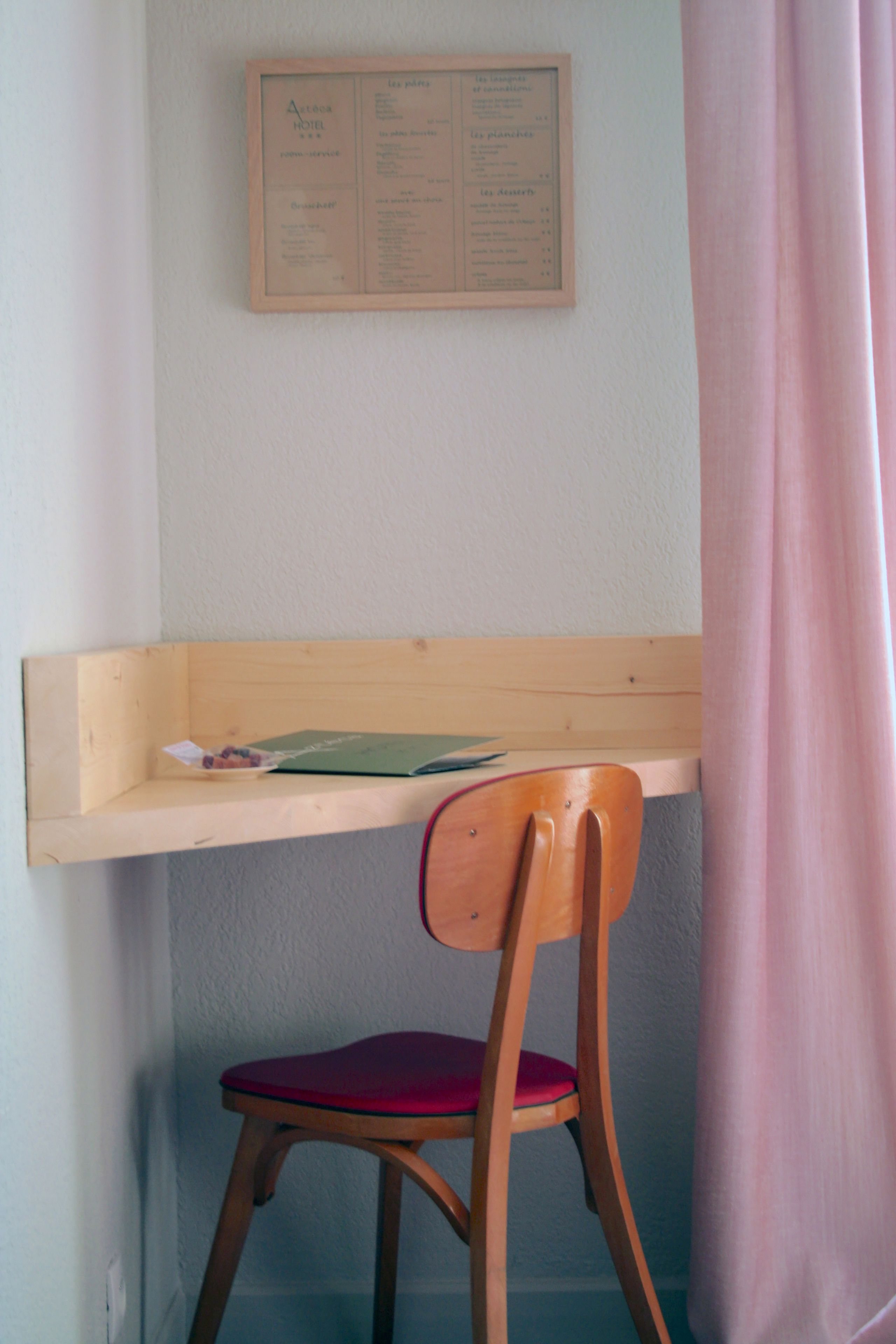 Un escritorio de madera con una silla, una pizarra de menú y una cortina.