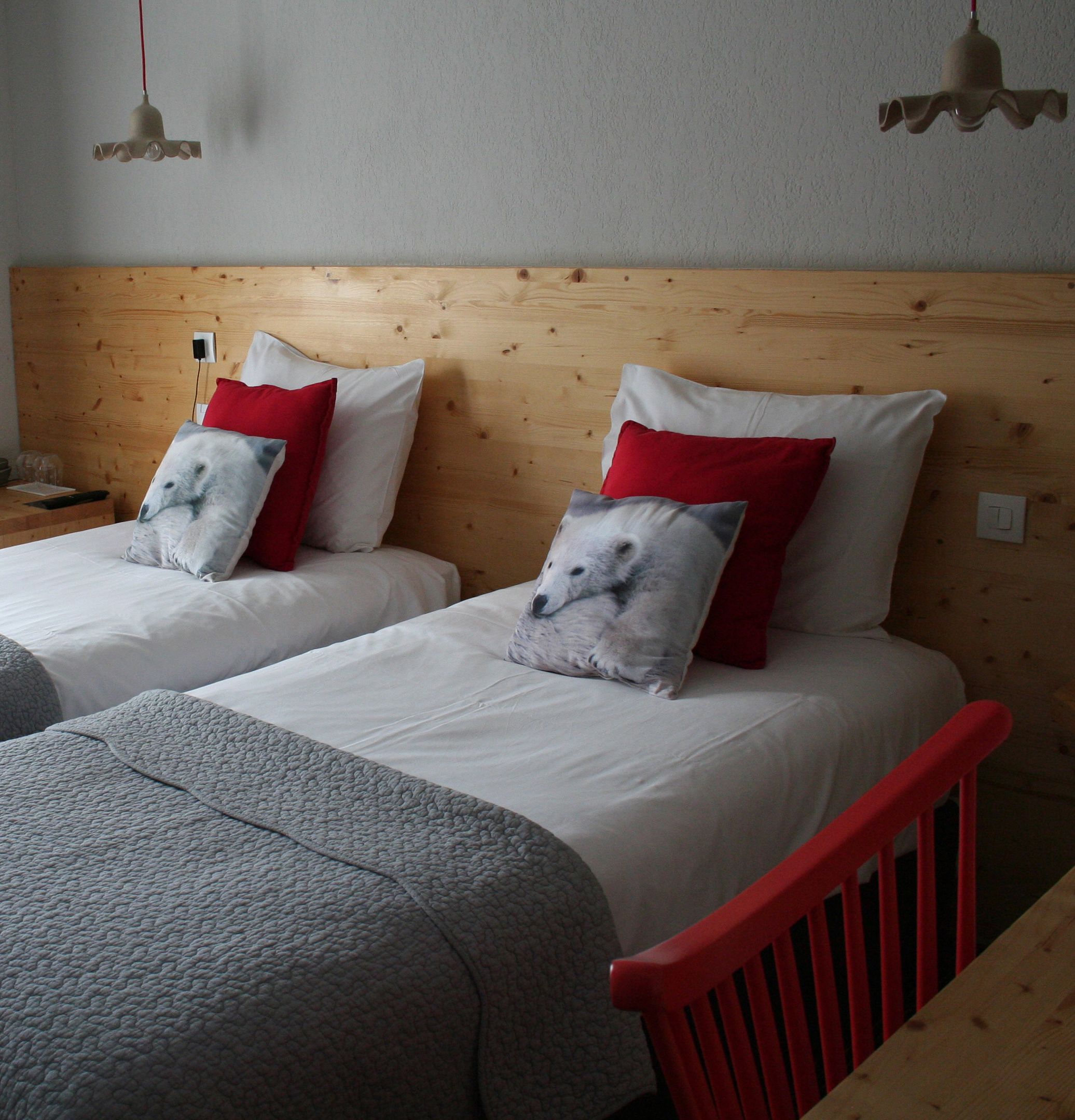 Two single beds with wooden headboards, white bedding, and red and grey pillows.