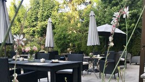 An outdoor patio with tables and chairs, surrounded by greenery and umbrellas. - Hotel Azteca (Barcelonnette)