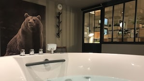 A hot tub with a bear mural, a glass door, and a plant in the background. - Hotel Azteca (Barcelonnette)