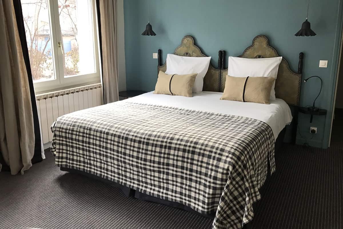 A neatly made bed with a checkered bedspread, two bedside lamps, and a window with curtains.