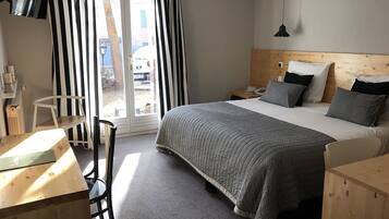 Une chambre d’hôtel avec un lit, un bureau, une chaise, une tête de lit en bois et une vue sur l’extérieur.