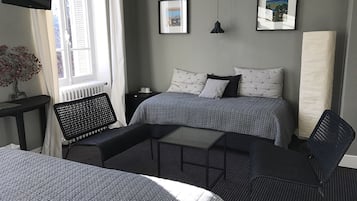 Et hotelværelse med to senge, et skrivebord, en stol, et fjernsyn og to billeder hængende på væggen.
