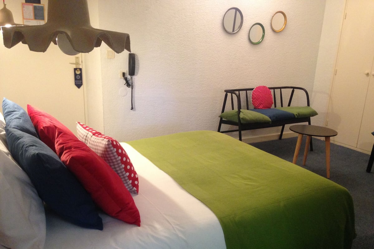 A neatly made bed with a green blanket, multiple pillows, and a telephone on the wall.