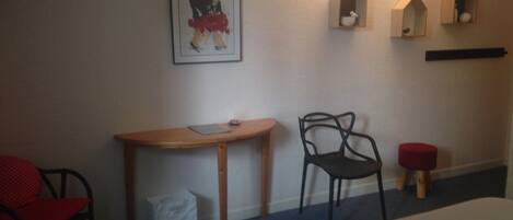 A hotel room with a bed, a desk, a chair, and a wall-mounted shelf with decorative items.