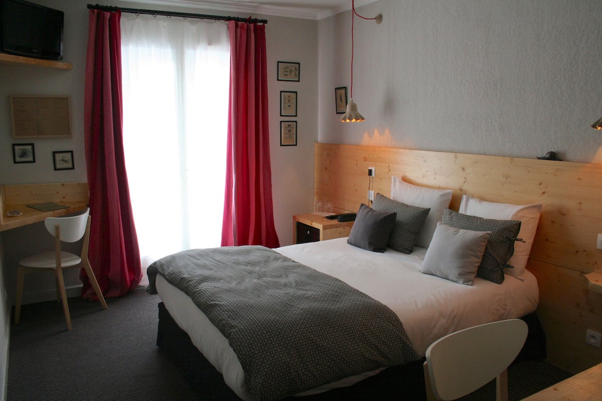 A neatly arranged hotel room with a bed, a desk, a chair, and a television on the wall.