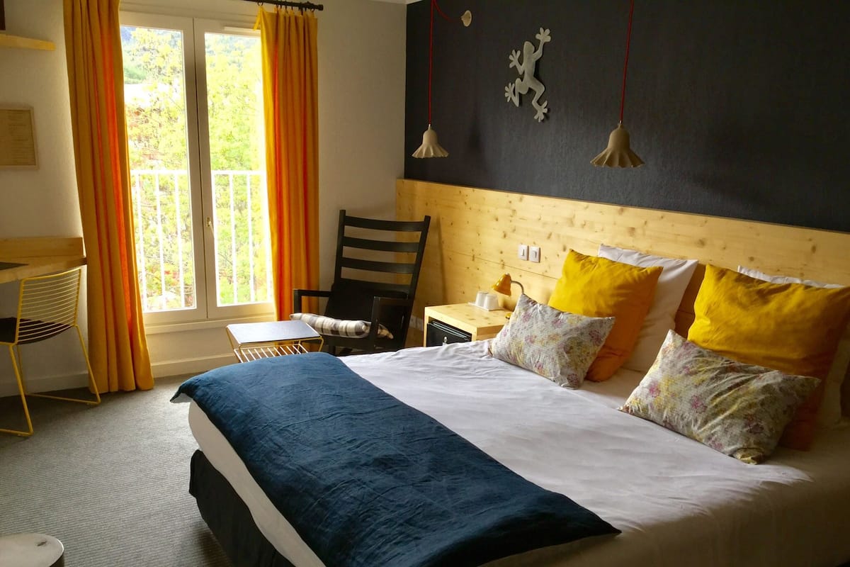 A bedroom with a bed, a desk, and a chair. There is a window with curtains.