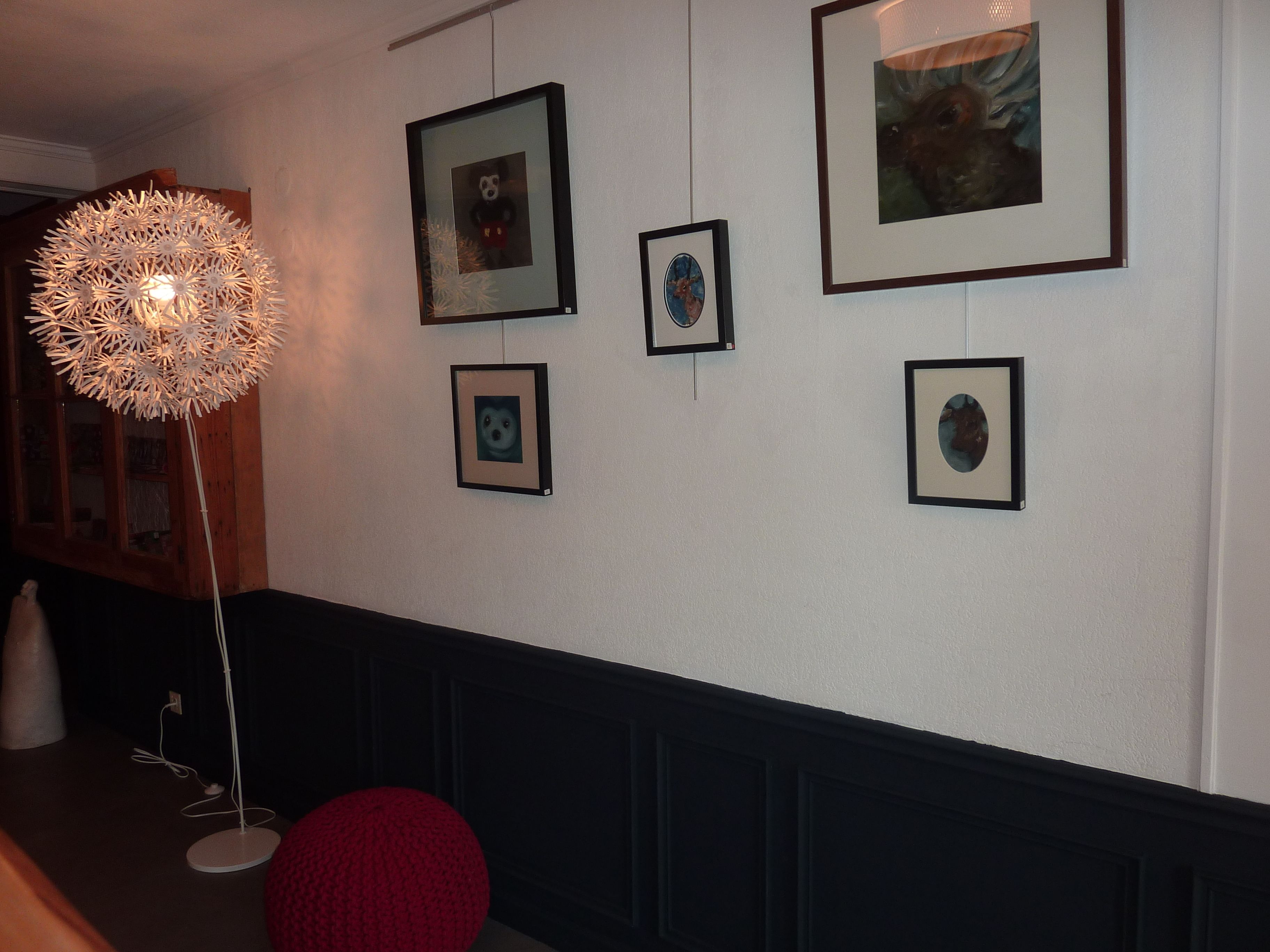 A hallway with framed artwork on the walls, a decorative light fixture, and a red chair.