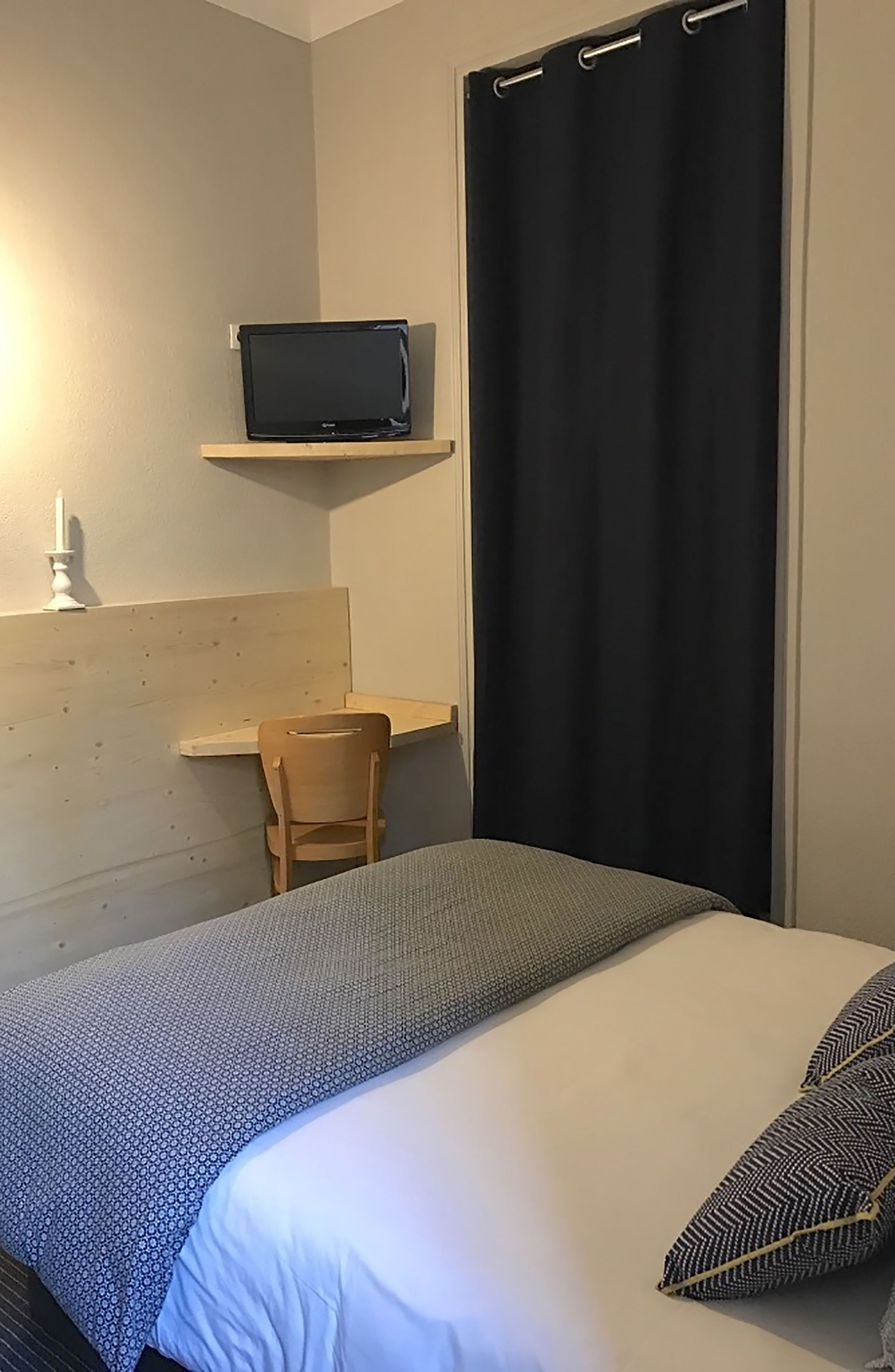 Makuuhuone, jossa on sänky, työpöytä kannettavalla tietokoneella, tuoli ja verho.