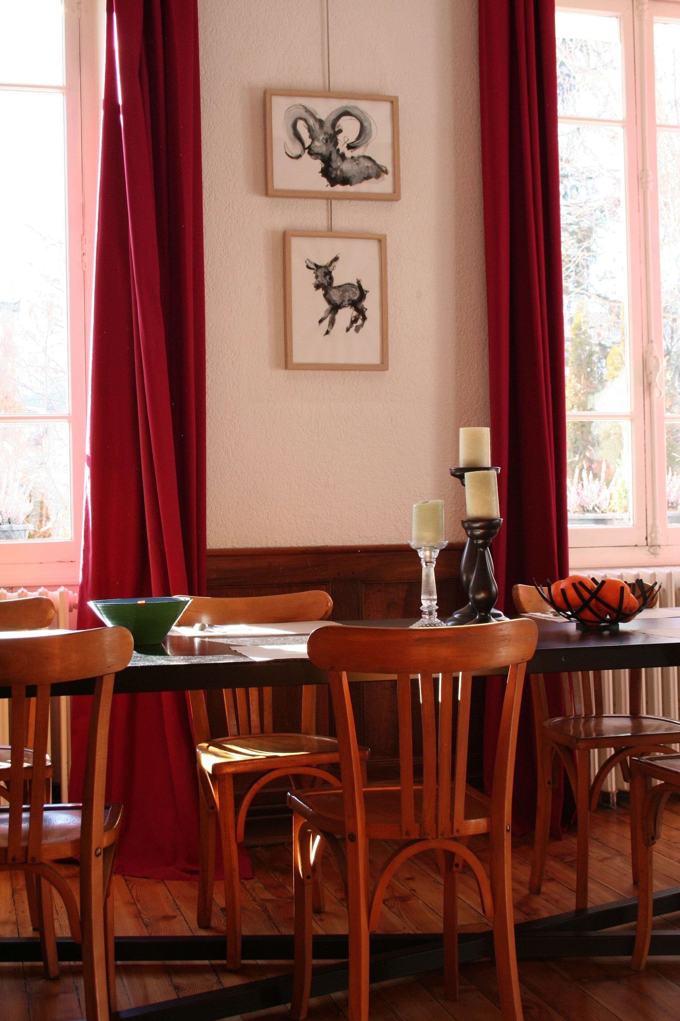 Un comedor con sillas de madera y una mesa, cortinas rojas y cuadros en la pared.