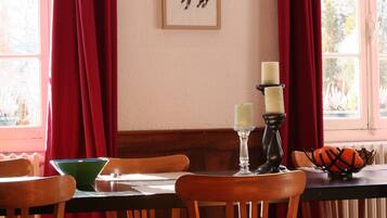 A dining area with wooden chairs and a table, red curtains, and framed artwork on the wall.