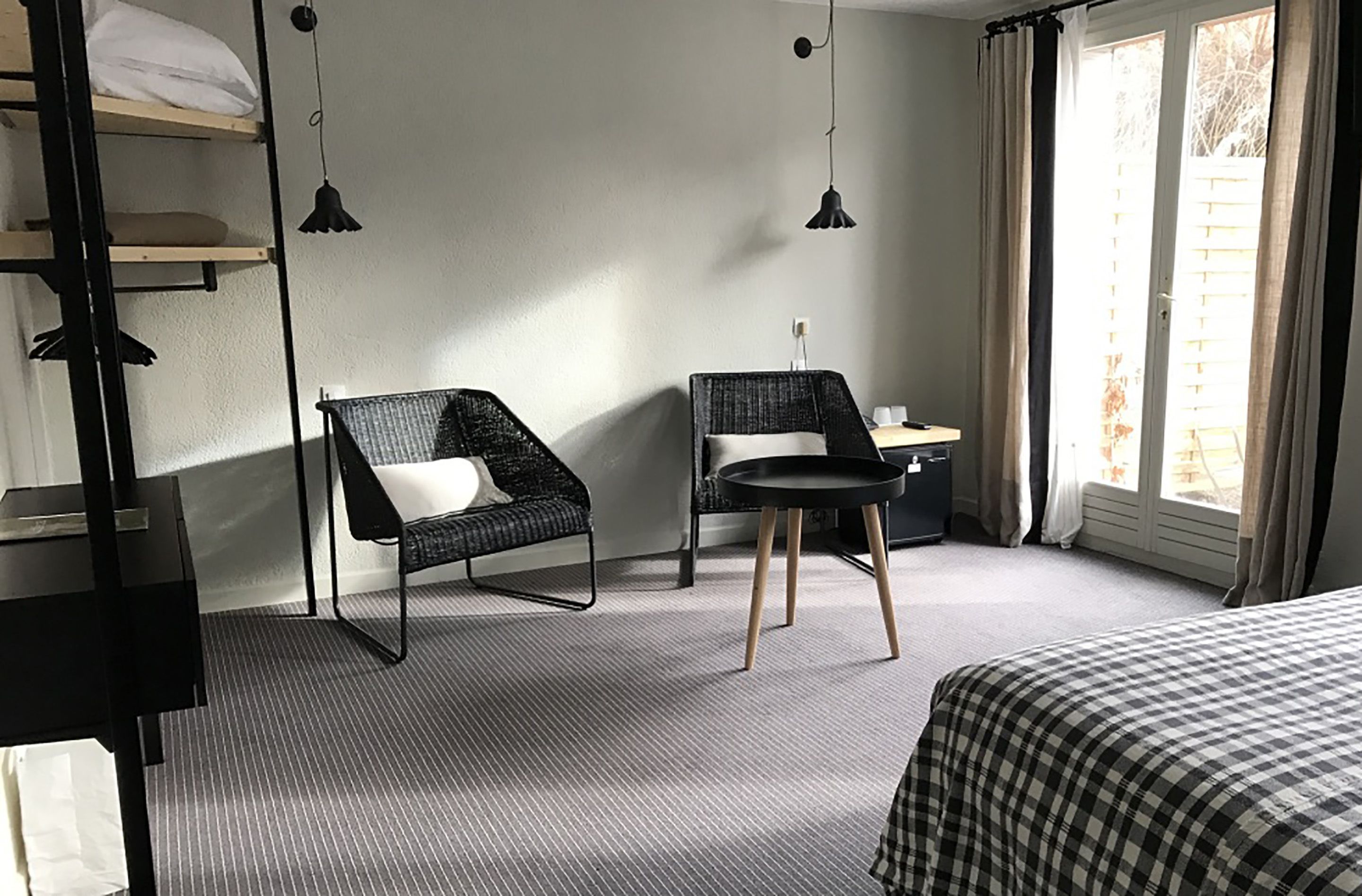 A hotel room with a bunk bed, two chairs, a small table, and a window with curtains.