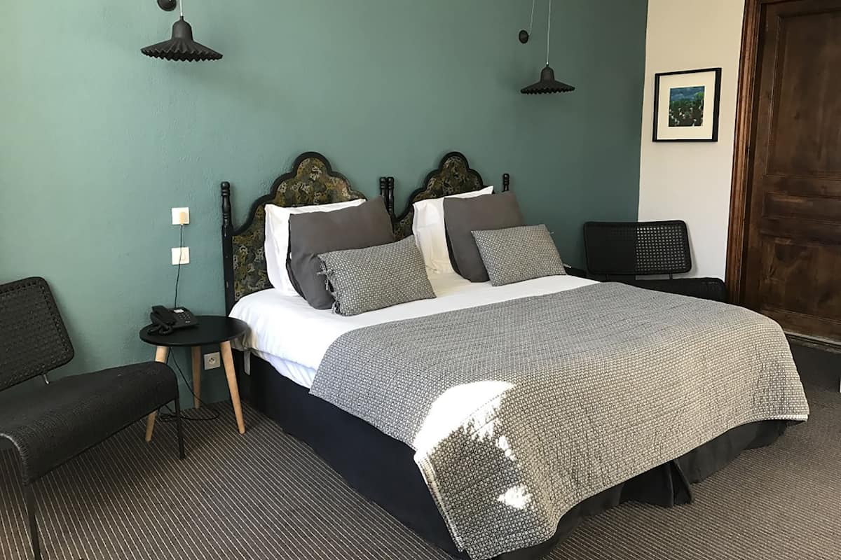 A neatly arranged bedroom with a large bed, bedside tables, a chair, and two hanging lamps.