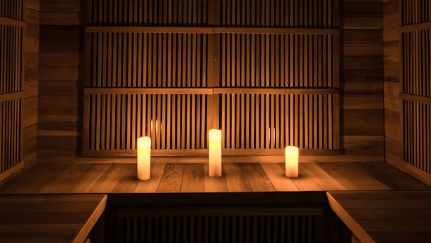 A wooden sauna with three lit candles on the floor, wooden benches, and a slatted wall design. - Hotel Azteca (Barcelonnette)