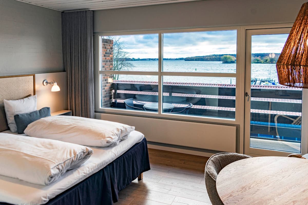 A hotel room with two beds, a view of a lake, and a balcony with outdoor seating.