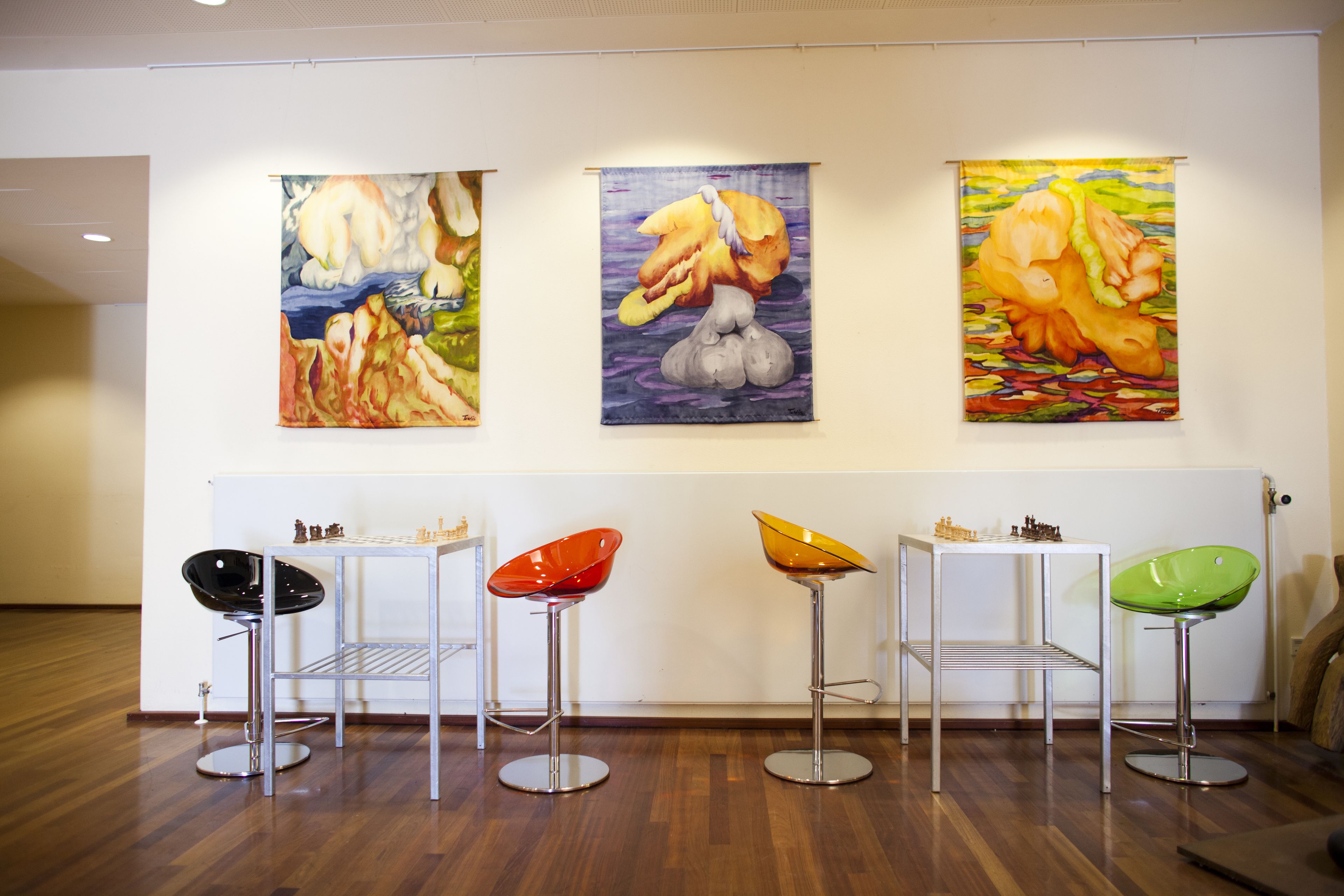 Una galería con tres cuadros y cuatro taburetes.