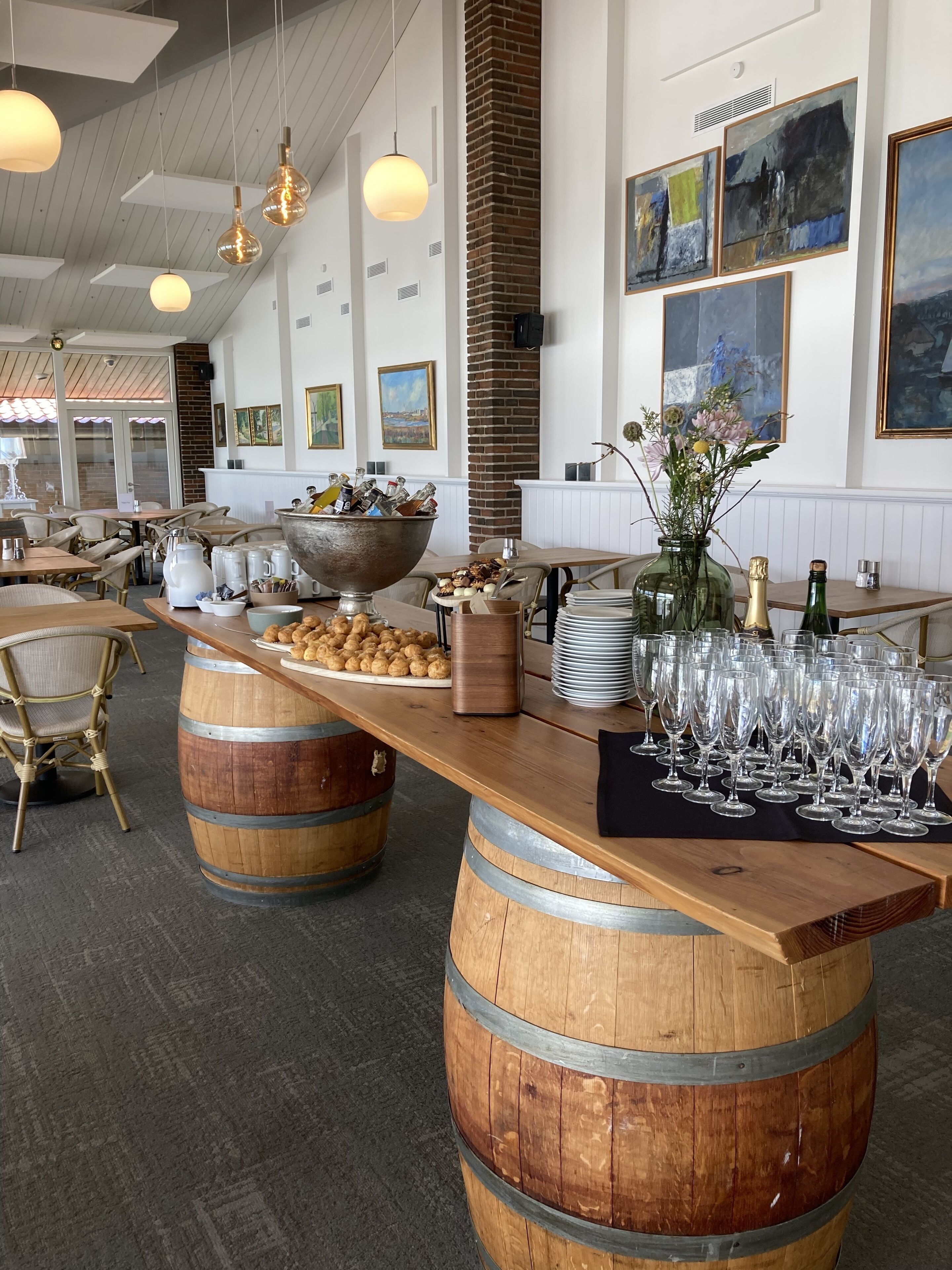 Un restaurant dont le bar est constitué de barils en bois, avec des tables et des chaises, et des lampes suspendues.