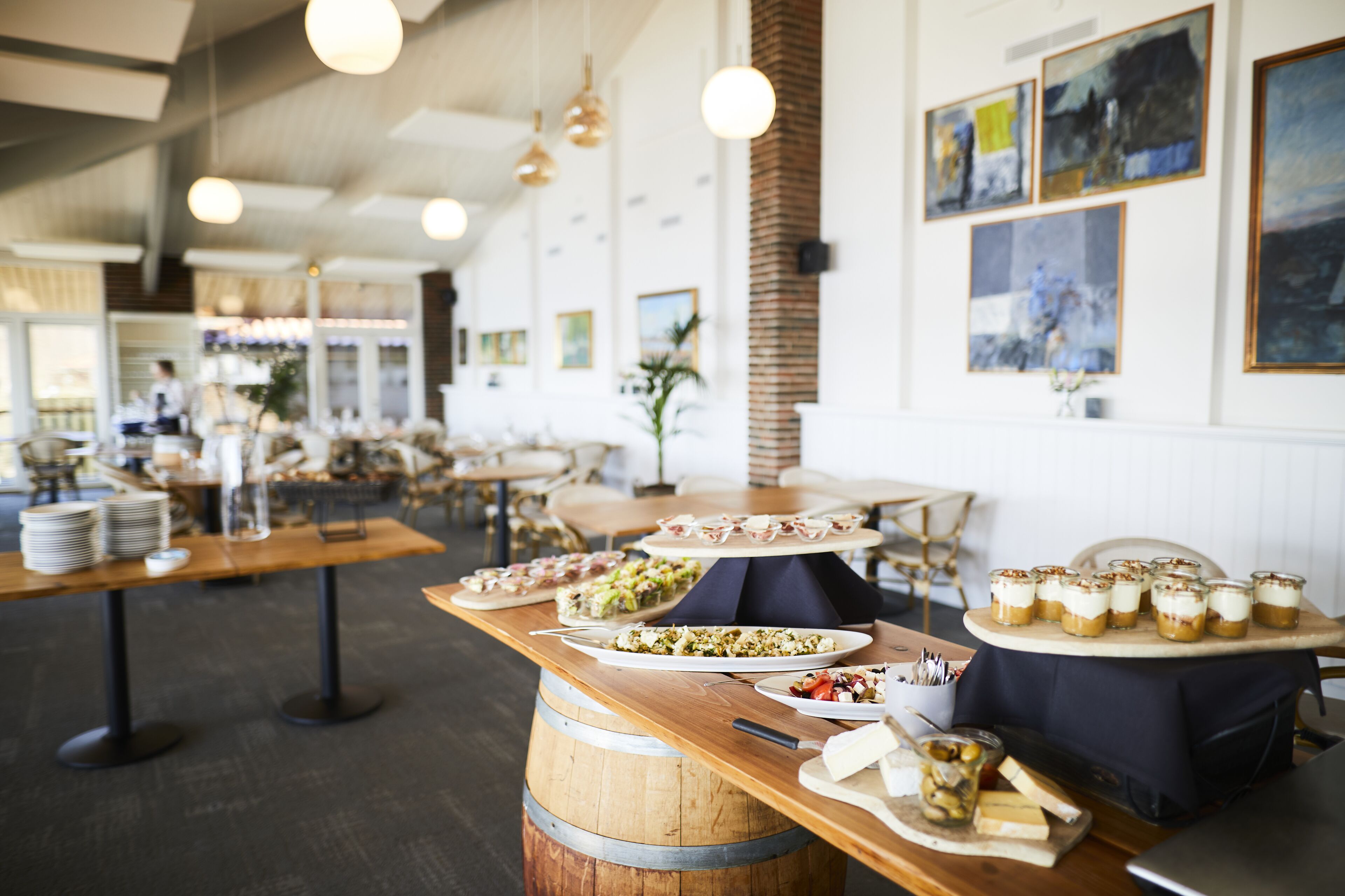 A restaurant with multiple tables, wooden barrels, and various food displays.