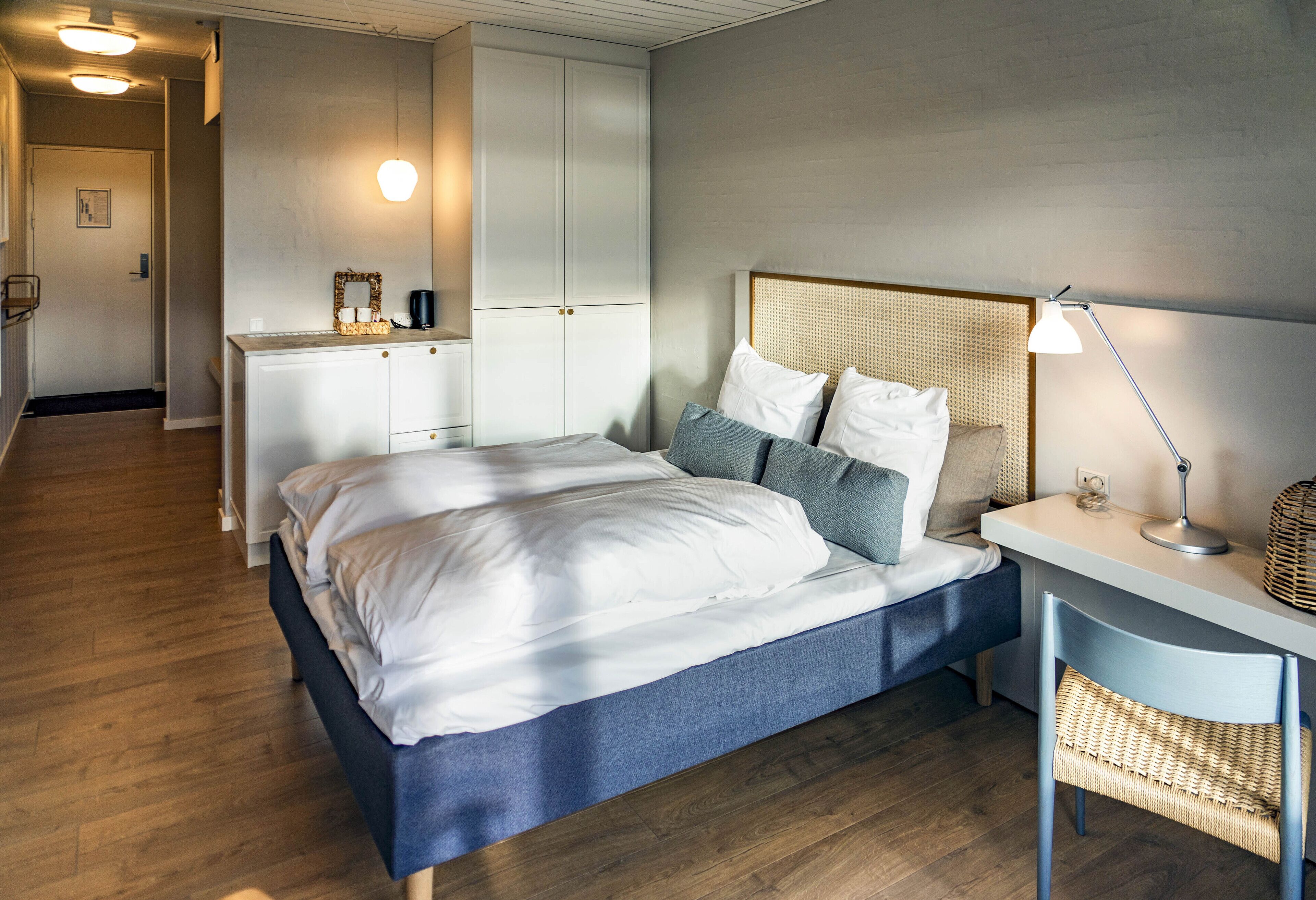 Un dormitorio con cama, mesita de noche, lámpara y escritorio con silla.