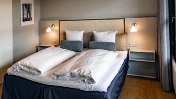Un lit bien fait, avec une tête de lit, deux tables de chevet avec des lampes et un tableau encadré au mur.