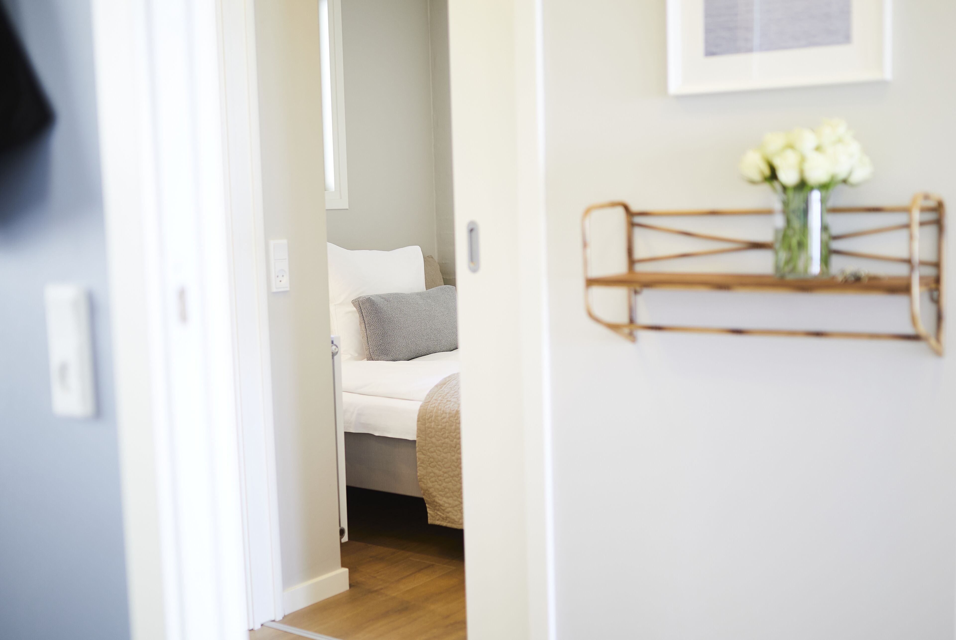 A bedroom with a bed, a bedside table, and a wall-mounted shelf with a vase of flowers.