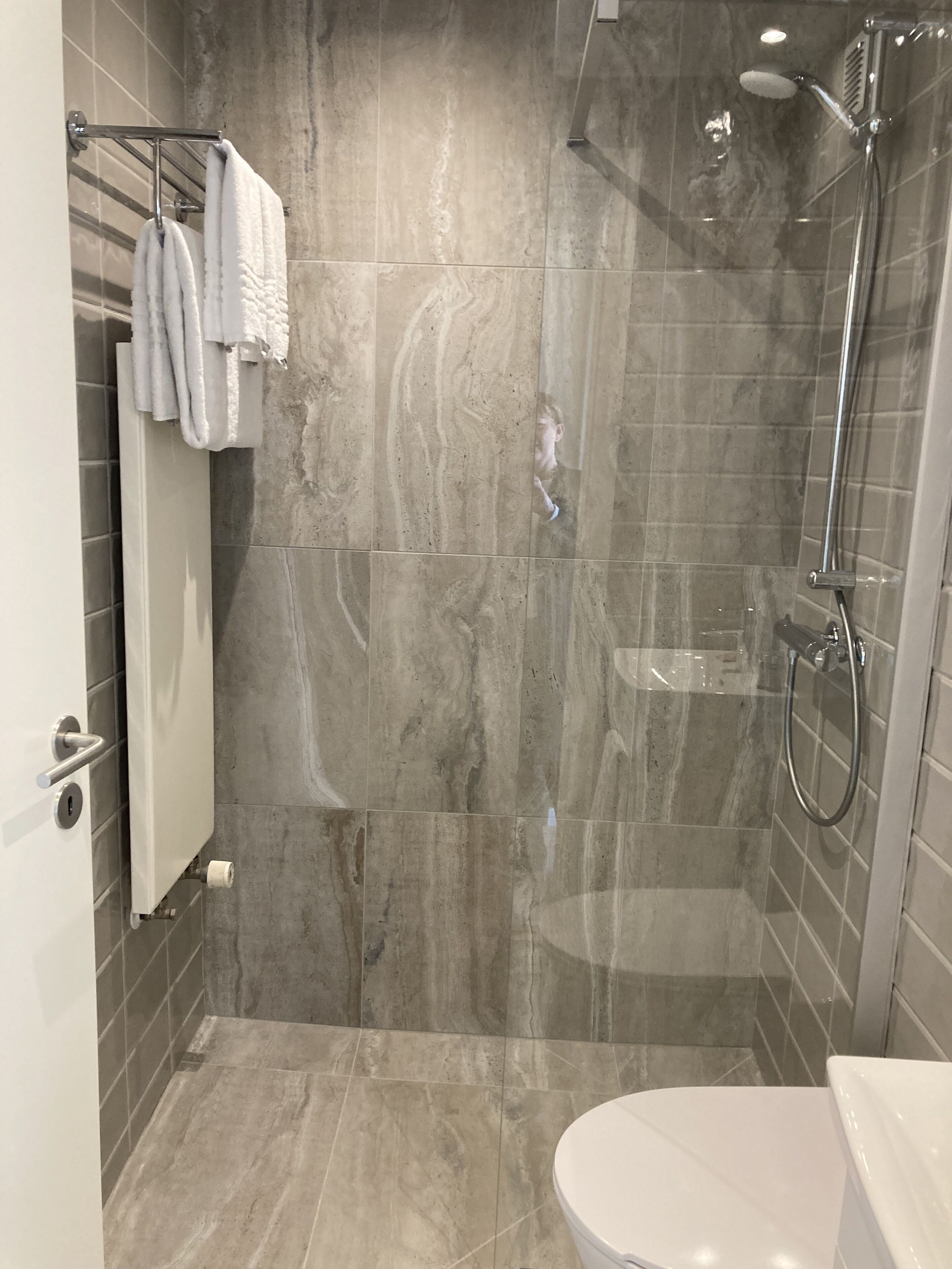 Een moderne badkamer met een douchecabine van glas, een toilet en een handdoekrek met witte handdoeken.
