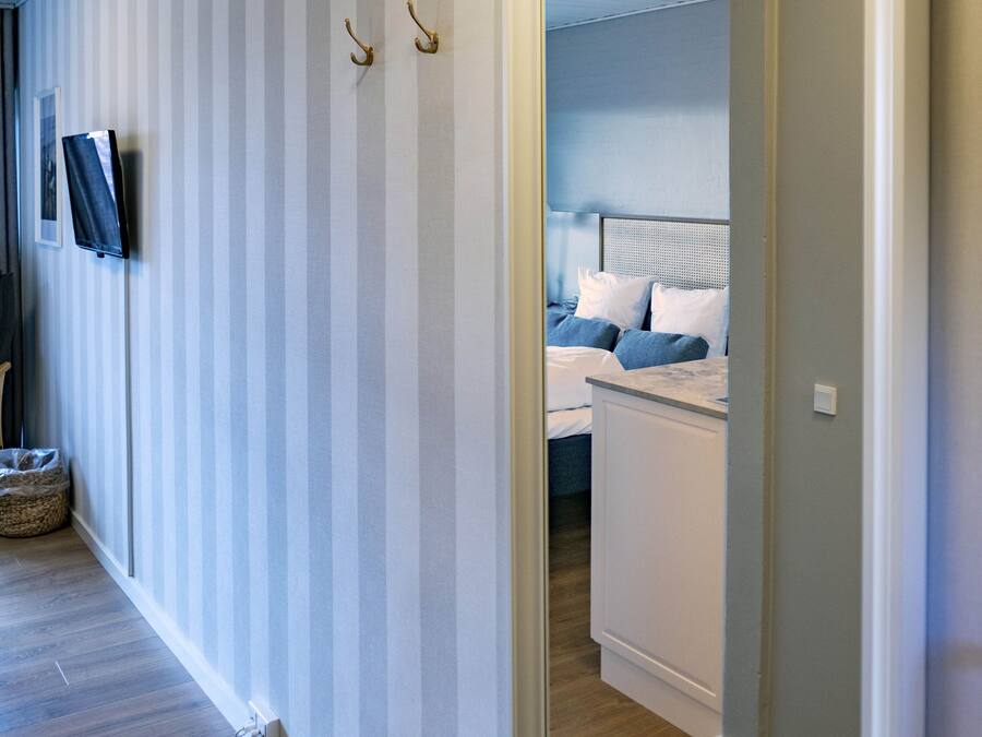 A hallway with striped wallpaper, a television mounted on the wall, and a bed with blue bedding in the background.